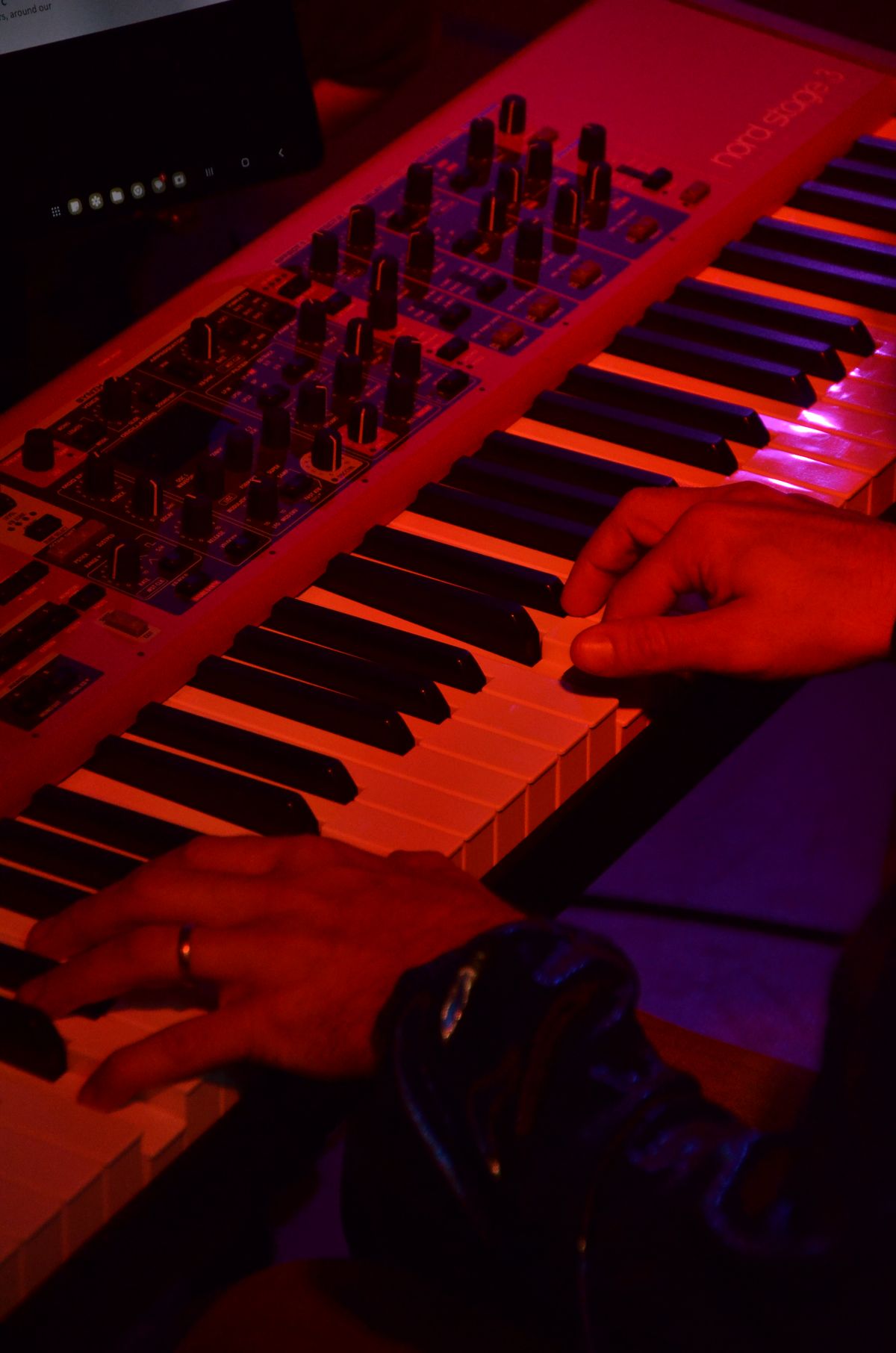 Mains sur le clavier d'un Nord Stage 3, en lumière rouge